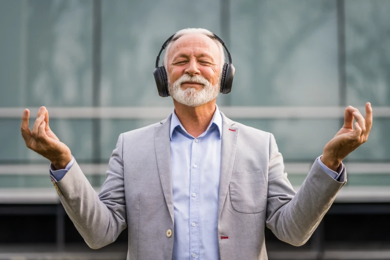 Älterer Mann im Anzug meditiert entspannt mit Kopfhörern und genießt Musik draußen.