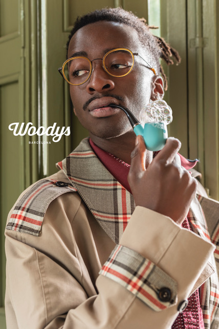 Junger Mann mit runder Brille und kariertem Trenchcoat raucht Seifenblasenpfeife.